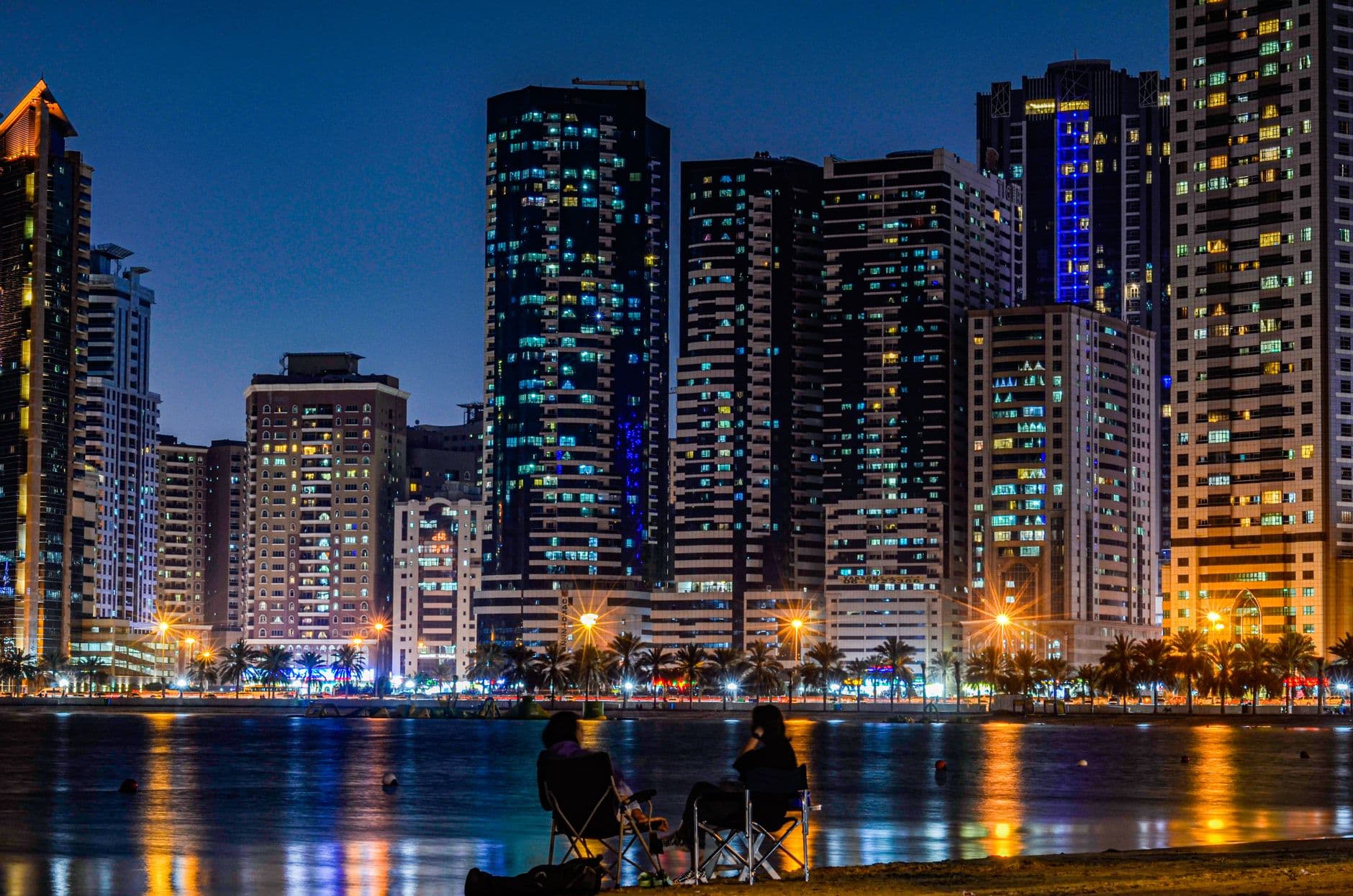 Beautiful night view of the Sharjah skyline with illuminated skyscrapers and waterfront reflections.