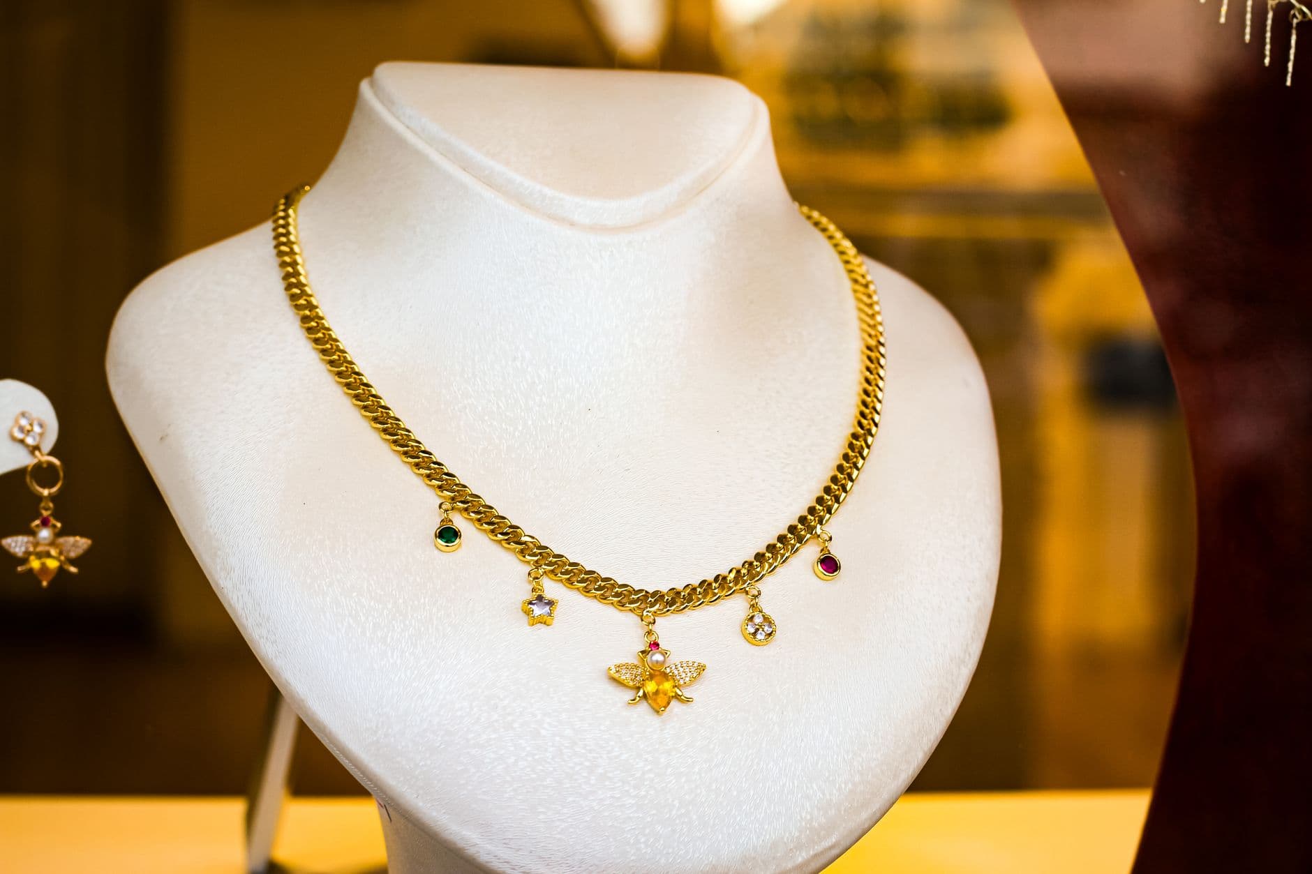 A gold necklace with gemstone charms elegantly displayed on a white bust in a jewelry store.