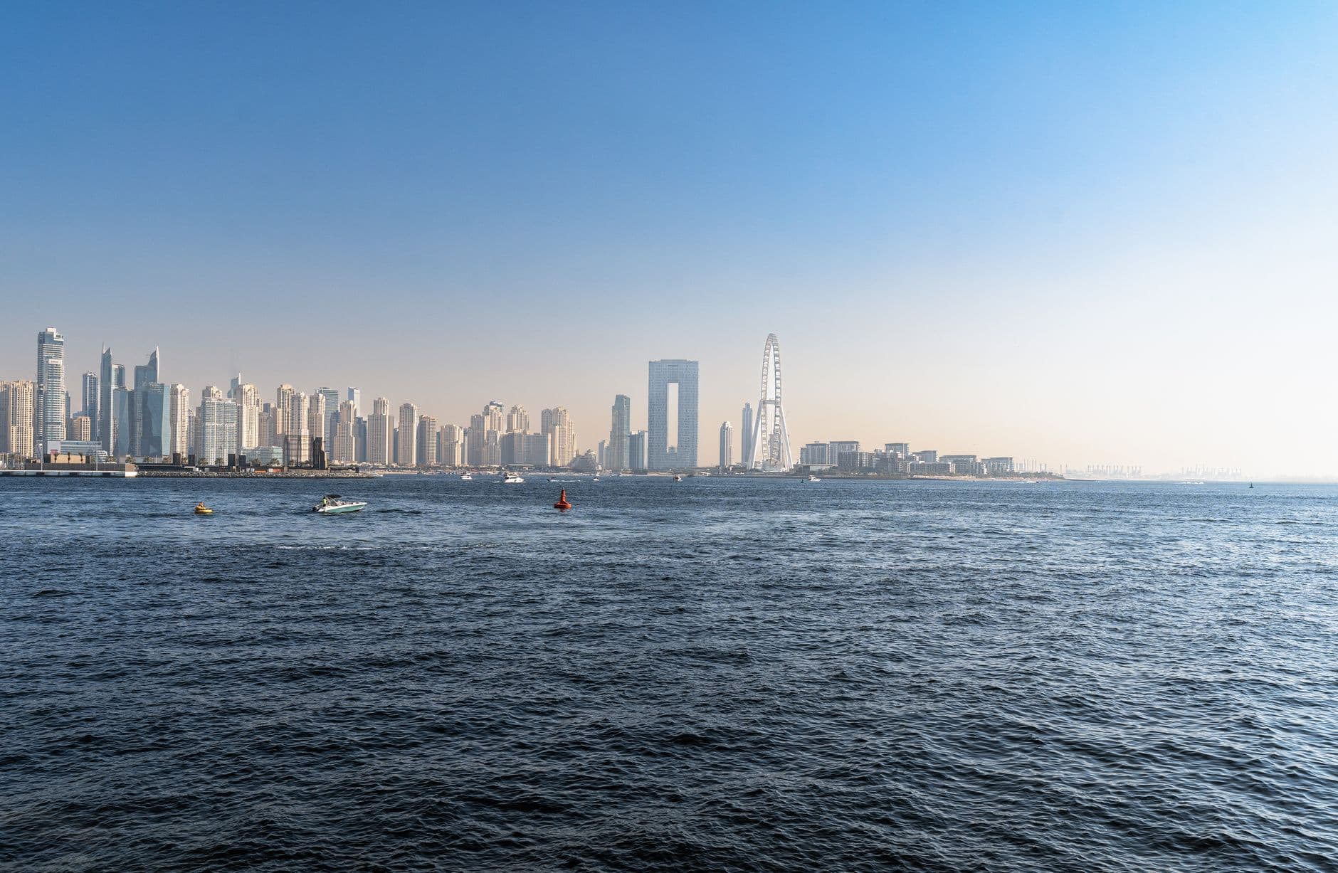 A stunning view of Dubai's skyline featuring skyscrapers, a Ferris wheel, and the vast sea under a clear blue sky.