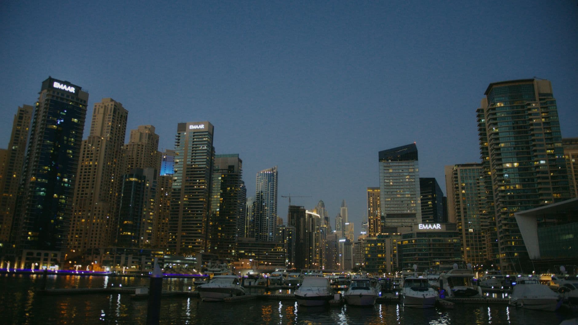 Stunning view of Dubai Marina's illuminated skyscrapers and yachts under a twilight sky.