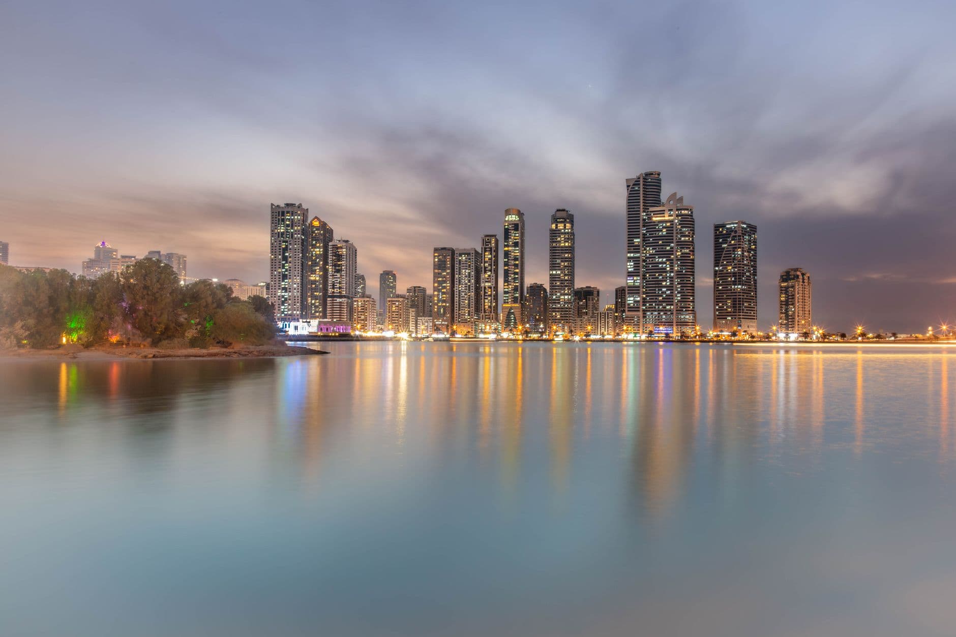 A breathtaking cityscape of Sharjah at sunset with reflections on the water, showcasing modern architecture.