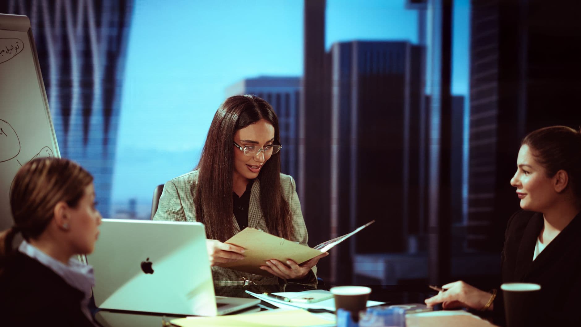 Three businesswomen engaged in a meeting at a Baghdad office with a city view.