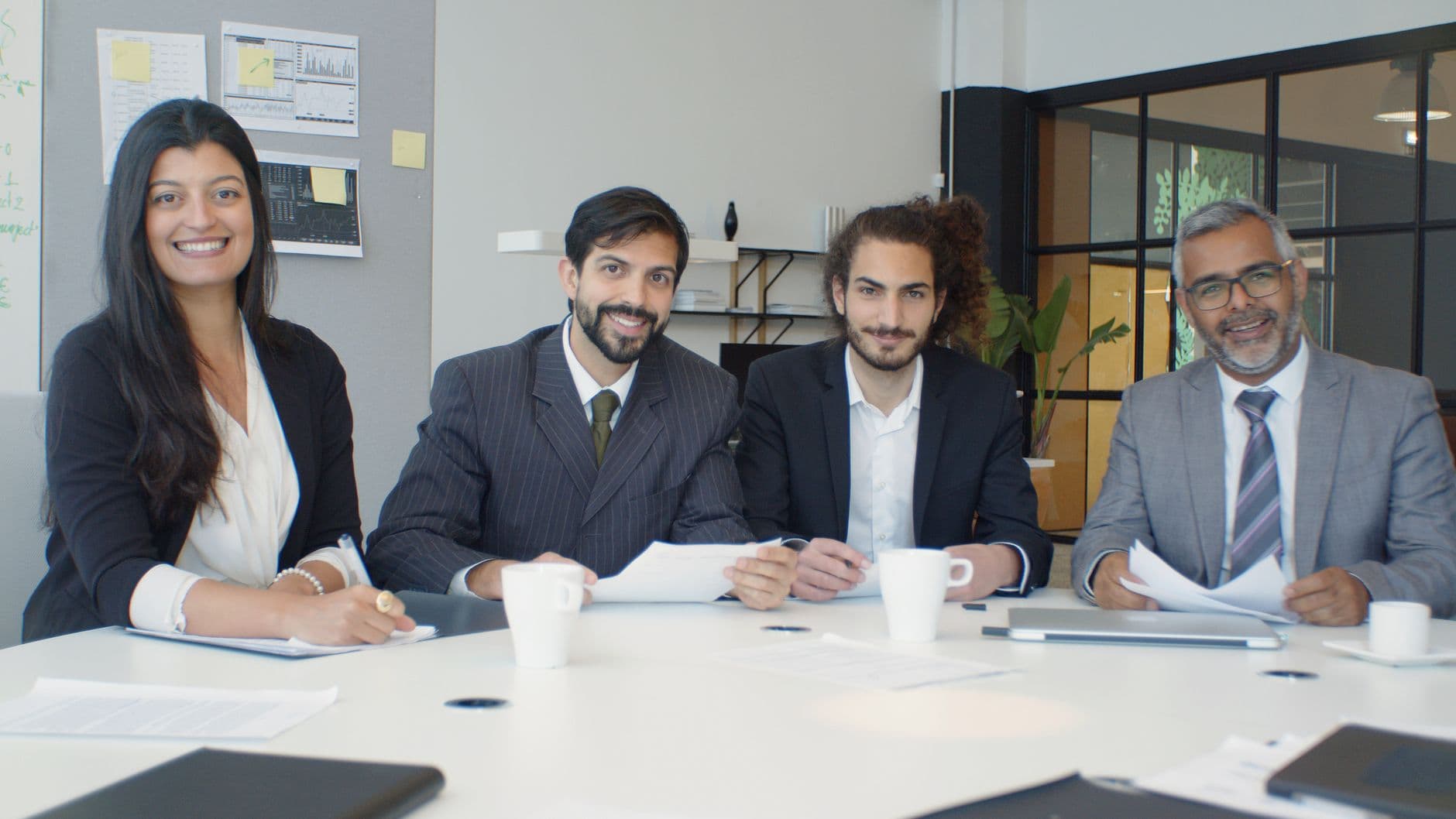 A diverse group of business professionals having a meeting in a modern office setting, engaged and smiling.